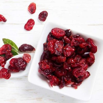 Photo of dried cranberries with leaves on white wooden surface; concept of superfood